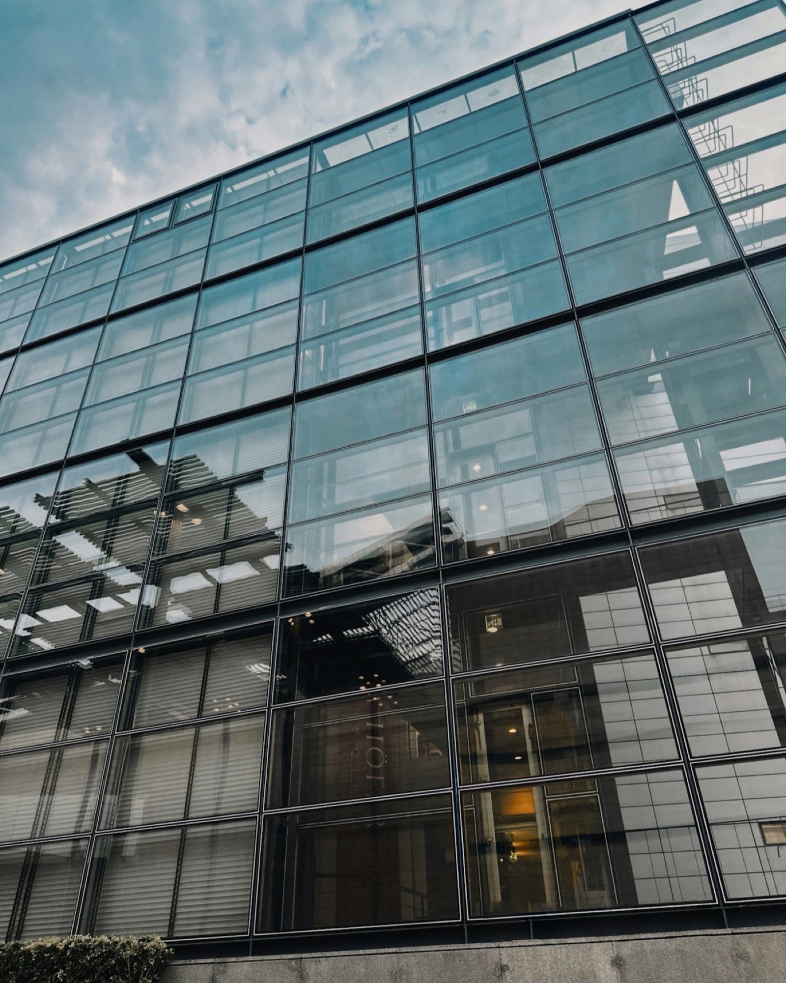 Glass office building seen from the street, reflecting the sky.