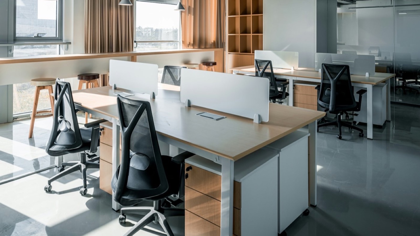 Open-plan office interior with desks and daylight from a wall of windows.